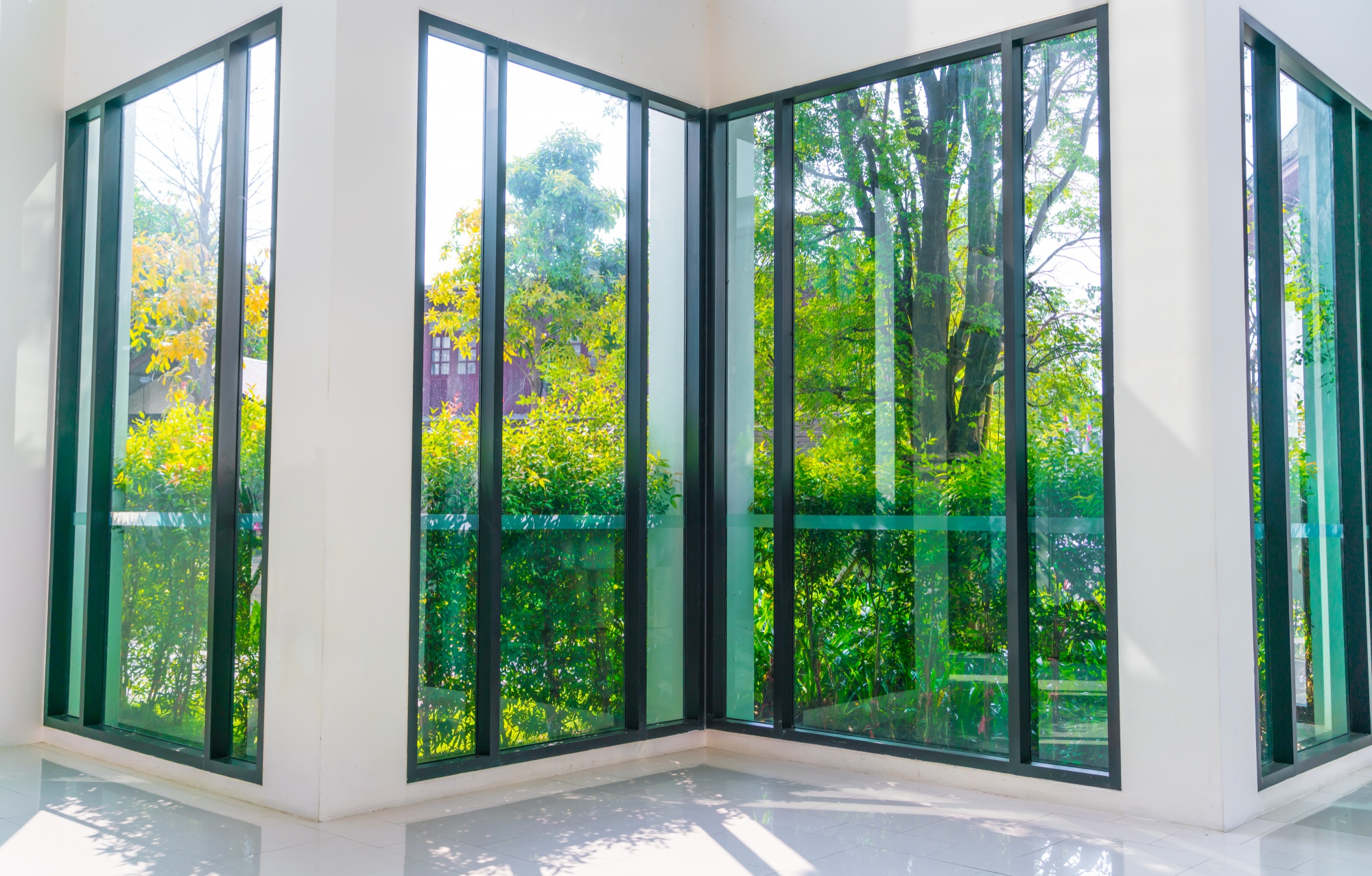 Corner of a room with floor-to-ceiling glass windows, garden outside.